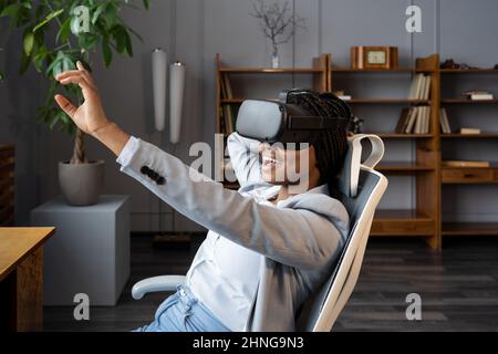 Amazed african woman in VR headset enjoying shopping in virtual reality during work break in office Stock Photo