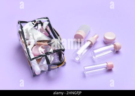 Empty travel bottles and bag with cosmetics on lilac background Stock Photo