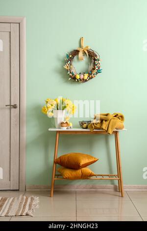 Table with beautiful tulips, knitted sweaters and stylish Easter decor near color wall in room Stock Photo