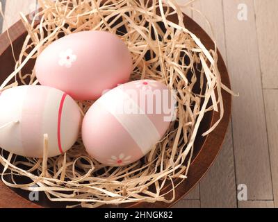 three pink Easter eggs in a nest on a wooden table, traditional Easter concept Stock Photo