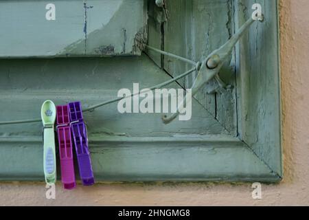 Old rural house pistachio green wooden window shutters with a matching shutter dog and hanging colorful clothespins in Nafplio, Greece. Stock Photo