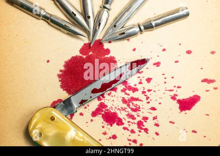 An army of Dip pen nibs and spilled red ink on a knife blade,  depicting the famous quote:  "a pen is mightier than a sword". Selective focus creative Stock Photo