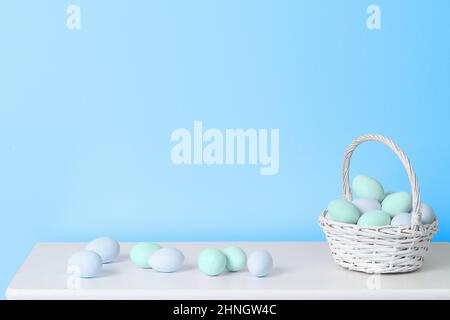 Basket with pastel blue and turquoise Easter eggs on white table near blue wall. Minimal Easter background Stock Photo