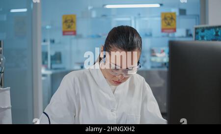 Woman chemist taking notes and using computer for experiment in laboratory. Specialist working on scientific development, doing research study and writing on paper in science lab. Stock Photo