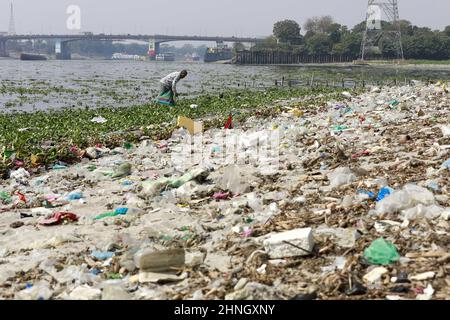 Dhaka, Bangladesh, February 16, 2022. A man collects discarded plastic items on the banks of the river Buriganga, in Dhaka, Bangladesh, February 16, 2022. Industrial waste and sewage from the city are all dumped into the rivers. The once fresh and flowing rivers like Buriganga, is now submerged in pollution. The other rivers of the country face the same fate. Recent research has brought an even more horrendous picture into view. And that is plastic pollution. In just the four rivers that surround the capital city Dhaka, 30,000 tonnes of plastic waste were discovered. Half of this was in the ri Stock Photo