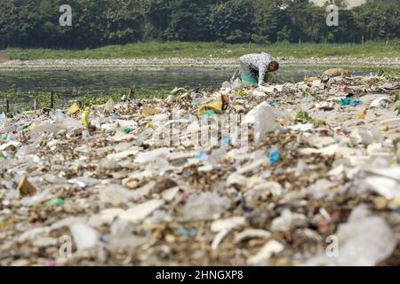 Dhaka, Bangladesh, February 16, 2022. A man collects discarded plastic items on the banks of the river Buriganga, in Dhaka, Bangladesh, February 16, 2022. Industrial waste and sewage from the city are all dumped into the rivers. The once fresh and flowing rivers like Buriganga, is now submerged in pollution. The other rivers of the country face the same fate. Recent research has brought an even more horrendous picture into view. And that is plastic pollution. In just the four rivers that surround the capital city Dhaka, 30,000 tonnes of plastic waste were discovered. Half of this was in the ri Stock Photo