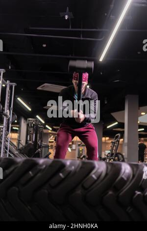 A man hits a sledgehammer wheel in fitness, the concept of a healthy lifestyle male sledgehammer active physical men, for gym equipment in training Stock Photo