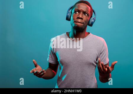 Man with thoughtful expression listening to music on headphones, having fun with modern audio sound. Pensive model using mp3 song on wireless earphones for enjoyiment and leisure activity. Stock Photo