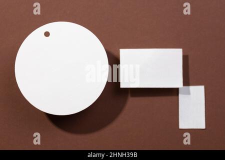 Three cardboard white colored brand blank tags of different shapes with circle on left and two rectangles on right put on brown background. Tag mock Stock Photo
