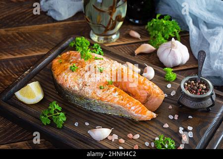 Baked salmon steak with herbs on wooden cutting board. Grilled salmon with salt and pepper Stock Photo