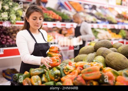 Spanish woman employee in vegetable store with green peppers Stock Photo