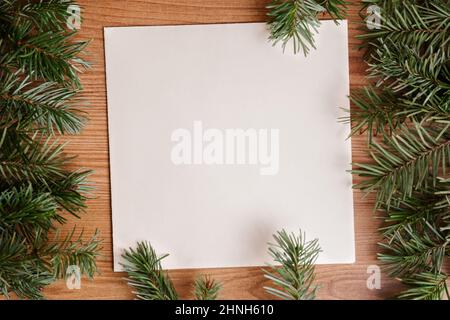 dark green lush pine fir branch frame on light brown wood and recycled white paper background fir leaves. Christmas tree or holiday card design for ec Stock Photo