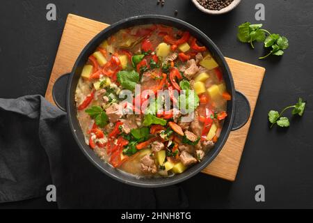 Homemade beef stew for winter dinner with vegetables, potatoes, pepper, carrot in bowl on black background. European cuisine. Top view. Stock Photo