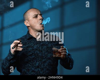 Mature businessman enjoying a glass of whiskey and a cigar in the evening after a day at the office Stock Photo