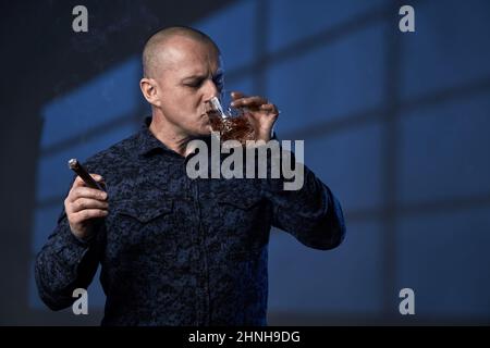 Mature businessman enjoying a glass of whiskey and a cigar in the evening after a day at the office Stock Photo