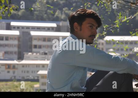 Close-up of a young guy looking sideways while sitting outdoor with buildings in background with copy space Stock Photo