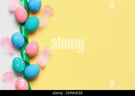 Easter composition on a yellow background. Colored eggs ribbon feathers. Top view flat lay border copy space Stock Photo
