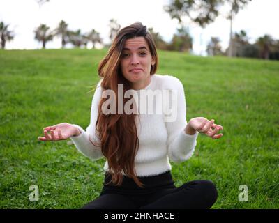 Young adult woman with a doubt shrugging shoulders in the park Stock Photo