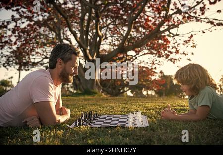 father and son playing chess on grass in park. fathers day. happy family. parenthood and childhood. Stock Photo