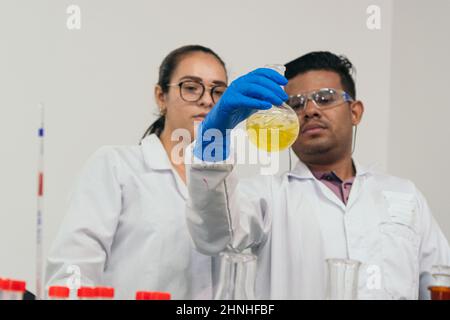 Serious lab workers holding a balloon in front of their eyes and examining the contents. Scientists wearing protective gloves, goggles and white coats Stock Photo