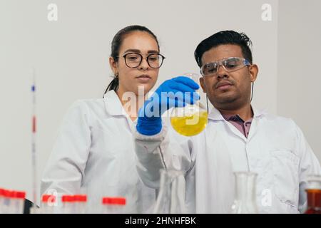 Serious lab workers holding a balloon in front of their eyes and examining the contents. Scientists wearing protective gloves, goggles and white coats Stock Photo