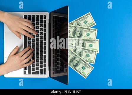 Female hands on laptop keyboard with money. Freelance concept, making money at home. Modern workspace, flat lay, blue background and top view Stock Photo