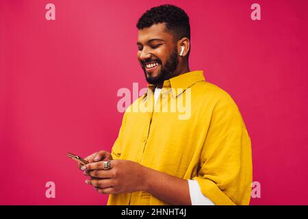 Browsing my favourite playlists. Happy young man using a smartphone while wearing wireless earphones. Carefree young man smiling cheerfully while stan Stock Photo
