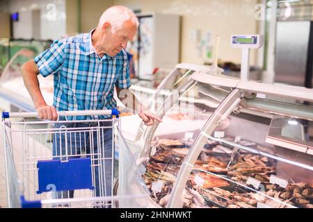 old age man examines smoked fish in department of supermarket Stock Photo