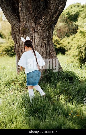 Easter egg hunt. Girl child Wearing Bunny Ears Running To Pick Up Egg In Garden. Easter tradition. Baby with basket full of colorful eggs. Bunny in basket Stock Photo