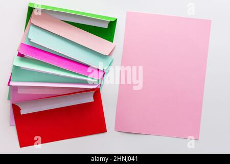 Multicolored envelopes with blank pink sheet of paper, greeting card or invitation mockup Stock Photo