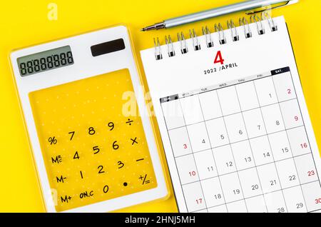 The April 2022 desk calendar with calculator and pen on yellow background. Stock Photo