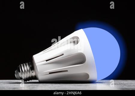 Glowing cold light LED bulb on the grey table on black background. Stock Photo