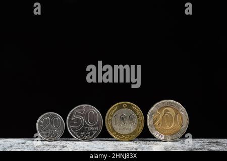 Kazakh coins in denominations of 20, 50, 100 and 200 tenge stand on a table on a black background with copy space. Stock Photo