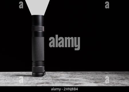 Flashlight stands on a table with beam of light upwards and copy space. Stock Photo