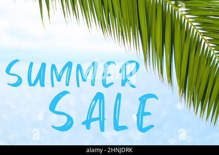 Summer sale message written in elegant font on the background with palm leaf and blue sea. Holiday concept and advertising of tour agency.  Stock Photo