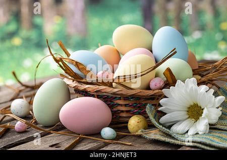 Colorful easter eggs in a basket and on a rustic wooden table with rural background Stock Photo