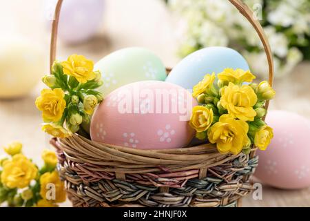 Closeup of colorful easter eggs and yellow flowers in a wicker basket Stock Photo