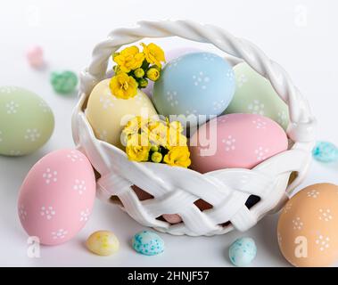 Colorful easter eggs, yellow flowers and candy in a basket and on a white background Stock Photo