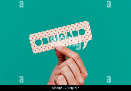 closeup of a man showing a paper speech bubble with the text thank you written in portuguese, on a green background Stock Photo