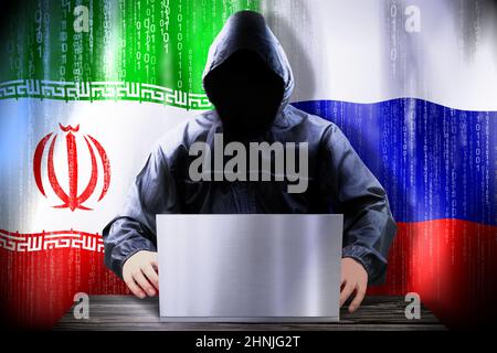 Anonymous hacker working on a laptop, flags of Iran and Russia Stock Photo