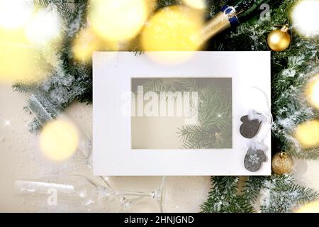 Christmas or New Year greeting card with fir tree branches with golden Christmas ball, glasses and bottle of Champagne, white paper frame. Golden boke Stock Photo