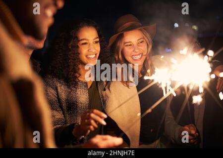 Multi-cultural best friends at a rooftop party smiling while lighting sparklers. Night time, stylish party Stock Photo