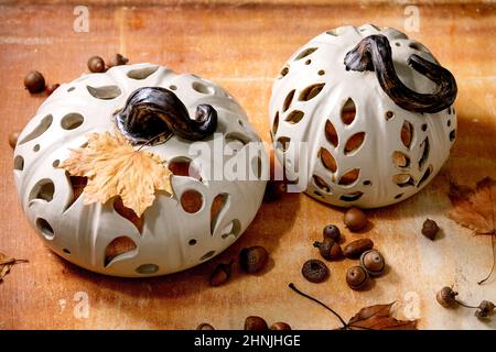 Halloween or Thanksgiving decorations, set of white handcrafted carved ceramic pumpkins standing on orange stone table with autumn leaves and acorns. Stock Photo