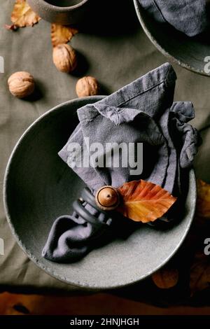 Rustic Autumn Halloween or Thanksgiving table setting with empty craft ceramic tableware, grey rough bowls and cups on linen tablecloth with autumn ye Stock Photo