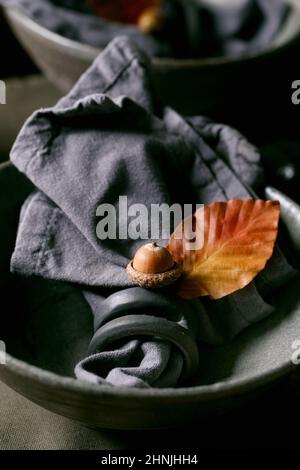 Close up of rustic Autumn Halloween or Thanksgiving table setting with empty craft ceramic grey rough bowls with textile napkin on linen tablecloth wi Stock Photo