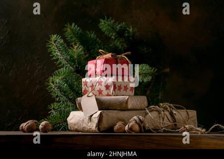 Collection of Christmas gift boxes in eco-friendly craft recycles paper decorated by natural nuts and cinnamon sticks on wooden table with fir tree br Stock Photo