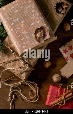 Collection of different Christmas gift boxes in eco-friendly craft paper decorated by natural nuts and cinnamon sticks over wooden background with fir Stock Photo