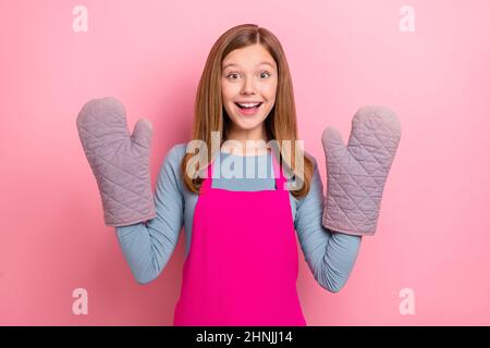 Portrait of attractive cheerful funny girl wearing apron gloves domestic culinary isolated over pink pastel color background Stock Photo