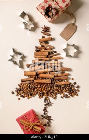 Aromatic spices cinnamon sticks and different coffee beans as Christmas tree shape and eco-friendly Christmas gift boxes over beige paper background. Stock Photo