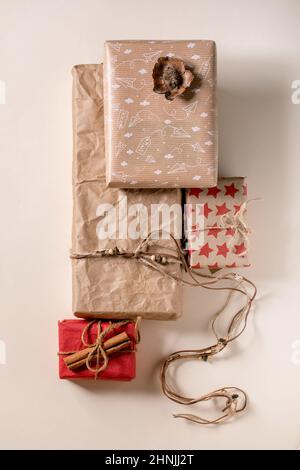 Collection of Christmas gift boxes in eco-friendly recycled craft paper decorated by cinnamon stick over beige paper background. Eco xmas gift concept Stock Photo